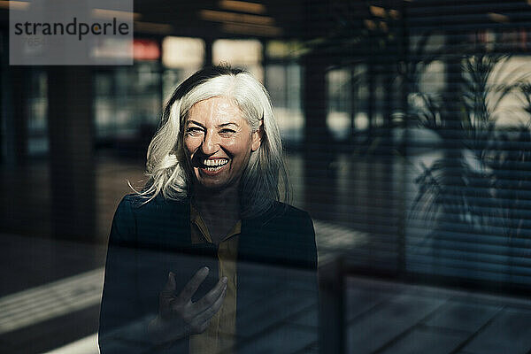 Cheerful woman with smart phone seen through glass