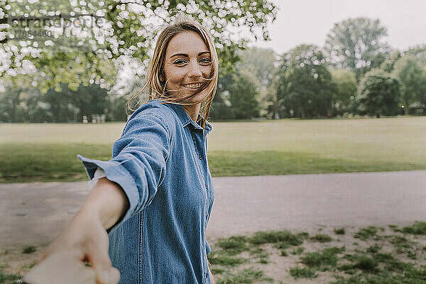 Lächelnde junge Frau zieht die Hand eines Freundes im Park