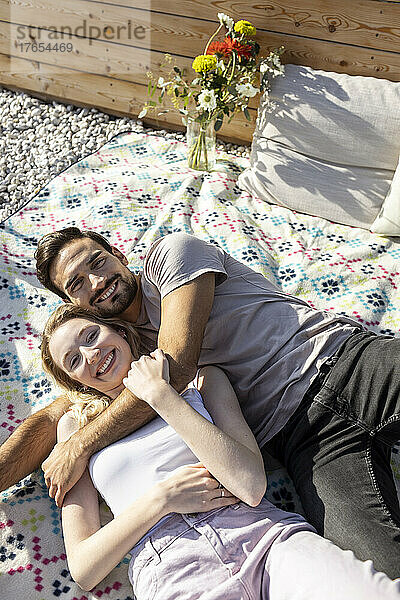Couple embracing each other lying down on picnic blanket at terrace