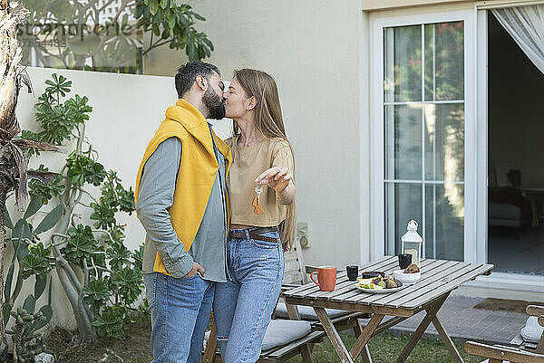 Mann küsst Frau mit Schlüssel am Haus im Hinterhof auf den Mund