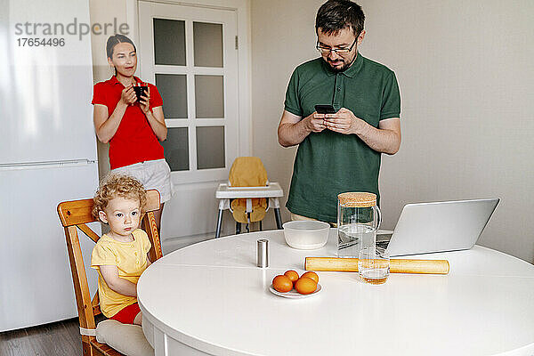 Woman looking at man using smart phone by daughter in kitchen