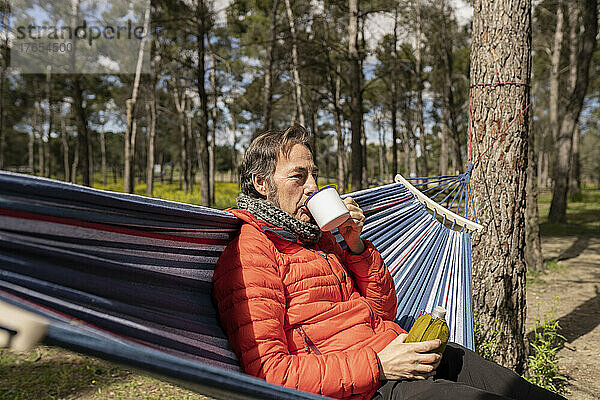 Reifer Mann trinkt Kaffee und sitzt an einem sonnigen Tag in der Hängematte