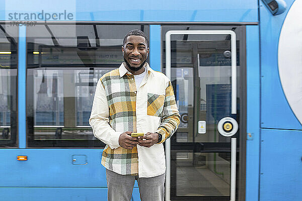 Lächelnder Mann mit Smartphone steht vor der Straßenbahn