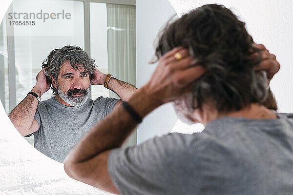 Älterer Mann mit Kopf im Haar  der in den Spiegel schaut