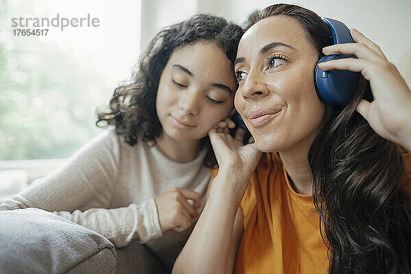 Lächelnde Frau  die zu Hause von ihrer Tochter Musik über Kopfhörer hört