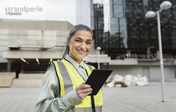 Glücklicher Ingenieur mit Tablet-PC  der vor einem modernen Gebäude steht