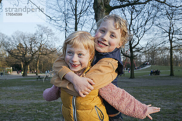 Verspielter Junge umarmt Schwester von hinten im Park