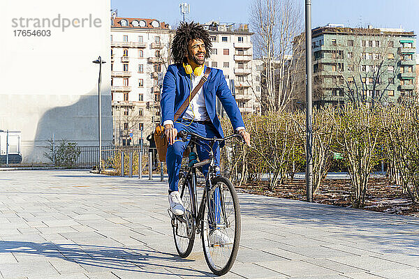 Glücklicher Geschäftsmann mit Umhängetasche fährt Fahrrad auf Fußweg