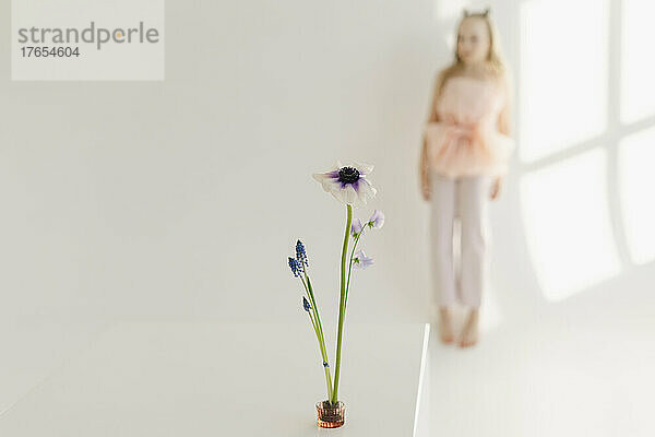 Frische Blume mit einem Mädchen  das vor einer weißen Wand steht
