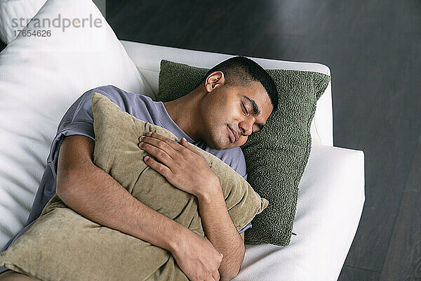 Young man with pillow sleeping on sofa in living room