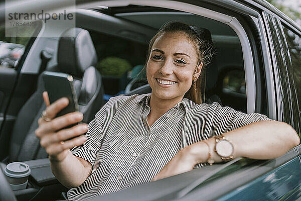 Glückliche Frau mit Smartphone sitzt auf dem Fahrersitz im Auto