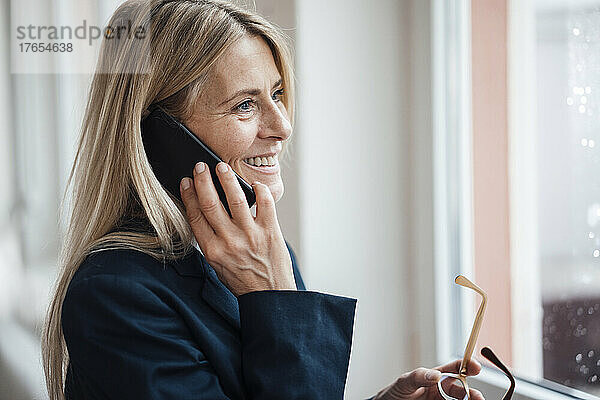 Lächelnde Geschäftsfrau  die am Arbeitsplatz mit dem Smartphone spricht
