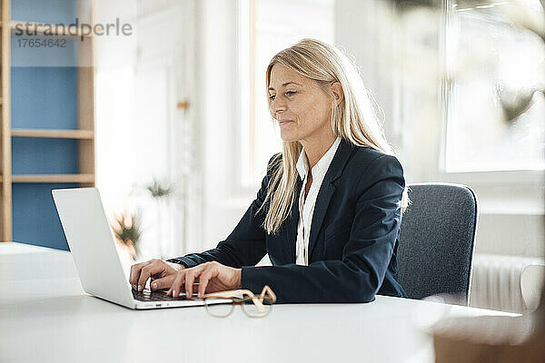 Blonde Geschäftsfrau benutzt Laptop am Schreibtisch am Arbeitsplatz