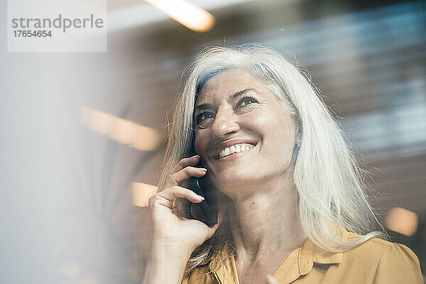 Glückliche Geschäftsfrau mit grauen Haaren  die im Büro mit dem Mobiltelefon spricht