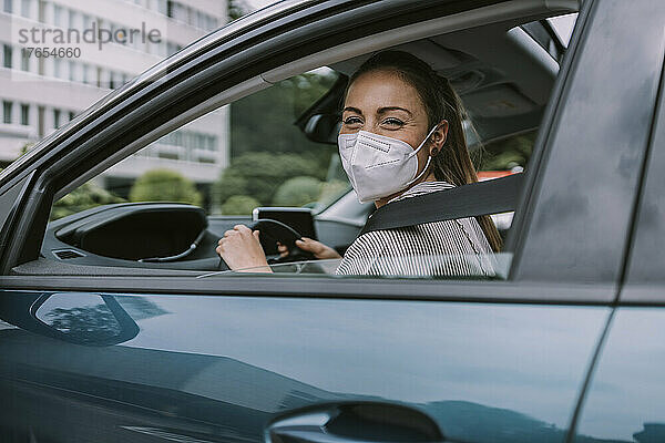 Junge Frau mit Schutzmaske schaut durch das Autofenster