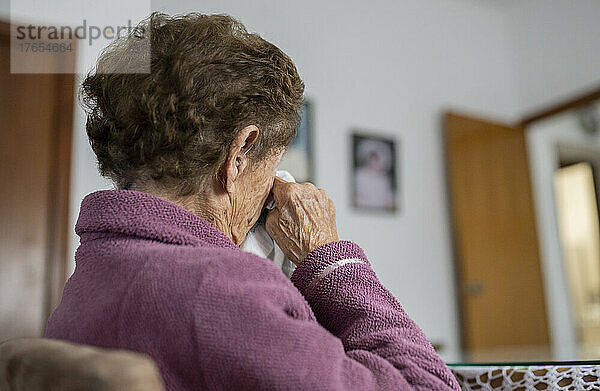 Ältere Frau reibt sich zu Hause die Augen mit Taschentuch