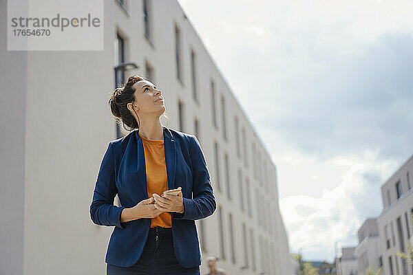 Geschäftsfrau mit Mobiltelefon steht an einem sonnigen Tag vor dem Gebäude