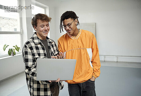 Lächelnder junger Mann  der Laptop mit Freund teilt