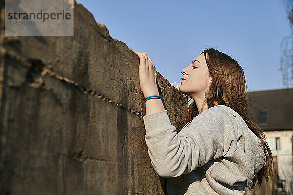 Neugierige junge Frau blickt über Betonmauer