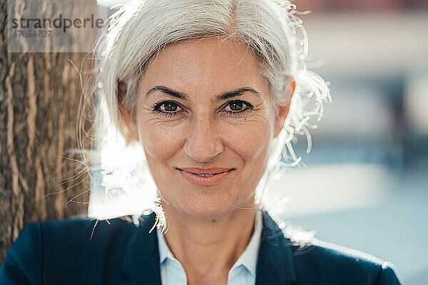Lächelnde Geschäftsfrau mit grauen Haaren an einem sonnigen Tag
