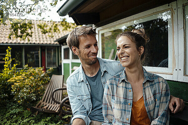 Lächelnder Mann blickt glückliche Freundin an  die im Hinterhof sitzt