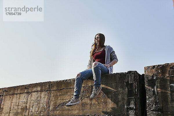 Young woman sitting on concrete wall looking at distance