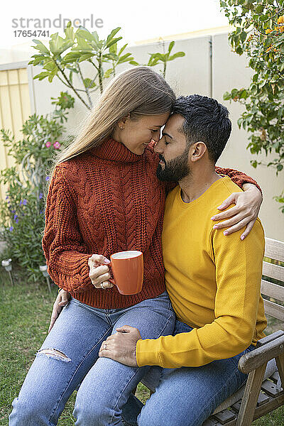 Woman with coffee cup sitting on man's lap in garden