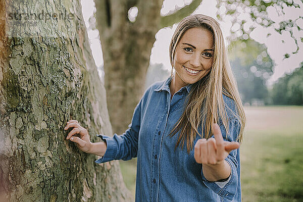 Lächelnde Frau gestikuliert am Baum im Park