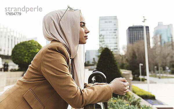 Junge Frau mit Hijab lehnt am Geländer im Büropark