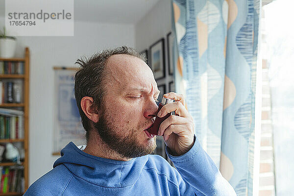 Mann mit geschlossenen Augen benutzt Asthmainhalator zu Hause