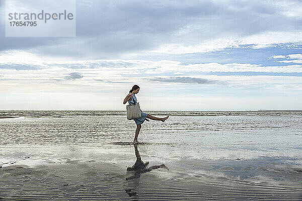 Mädchen mit Tasche spielt im Wasser am Strand