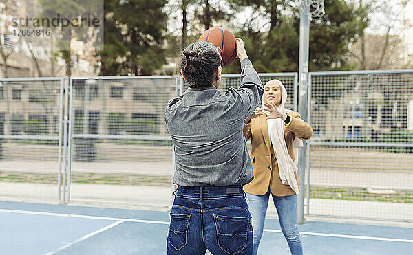 Geschäftsfrau spielt mit jungem Kollegen Basketball auf Sportplatz