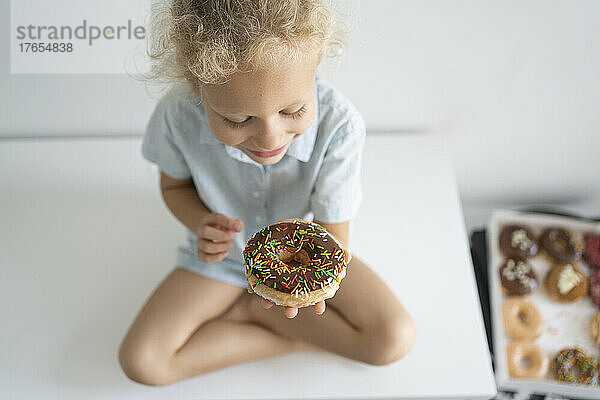 Lächelndes Mädchen mit Donut sitzt im Schneidersitz auf dem Tisch
