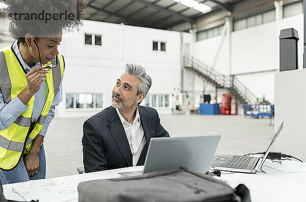 Geschäftsmann mit Laptop diskutiert mit Techniker am Schreibtisch in der Fabrik