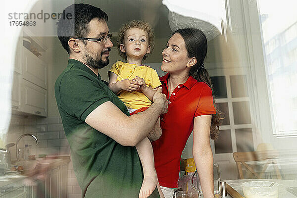 Smiling parents looking at cute daughter seen through glass window
