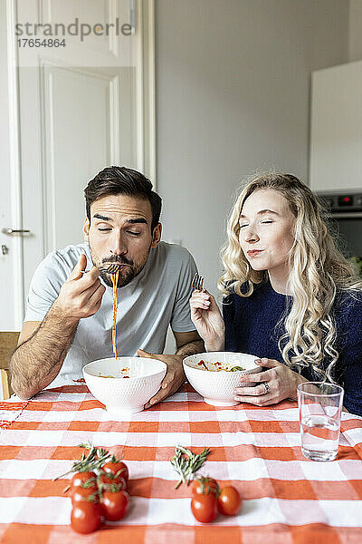 Hungriges Paar isst zu Hause Nudeln am Esstisch