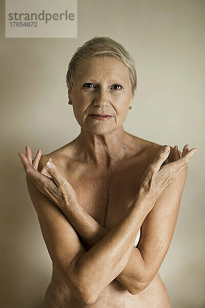 Topless senior woman covering breasts against white background