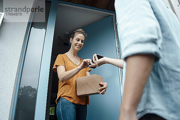 Lächelnde Frau mit Paketsignierung auf Smartphone  das vom Zusteller gehalten wird