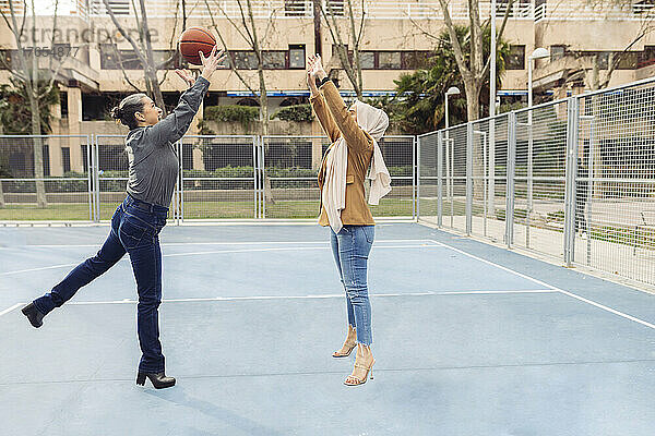 Geschäftsfrau wirft einem Kollegen  der auf dem Sportplatz springt  Basketball zu