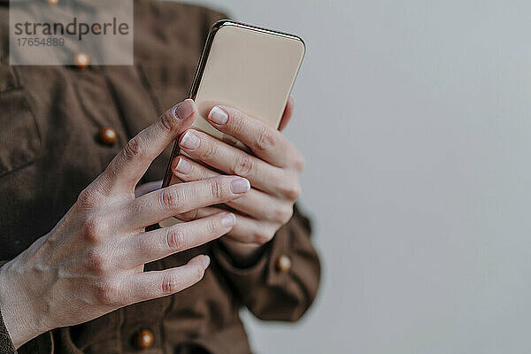 Hand einer Frau  die ihr Mobiltelefon vor grauem Hintergrund hält