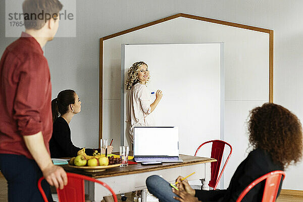 Lächelnde Geschäftsfrau erklärt Kollegen im Projektraum im Büro die Geschäftsstrategie
