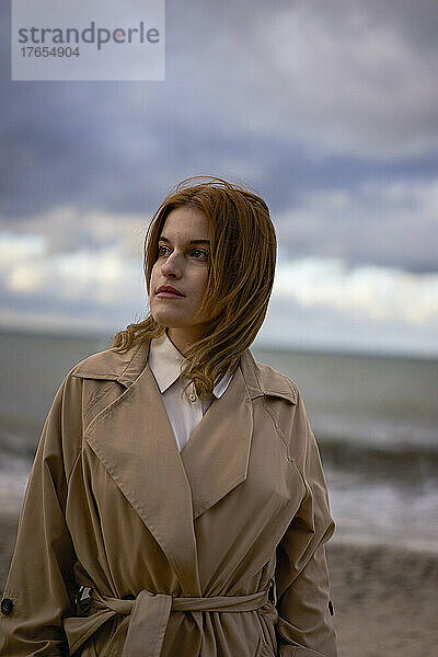 Schöne junge Frau im Mantel steht am Strand