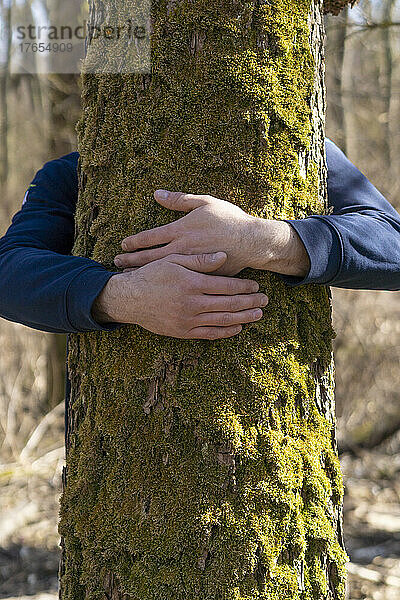 Junger Mann umarmt Baum an sonnigem Tag