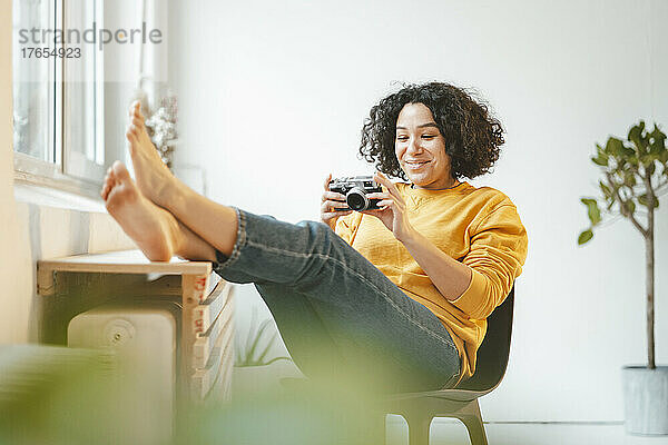 Lächelnde Frau mit Kamera  die zu Hause auf einem Stuhl sitzt