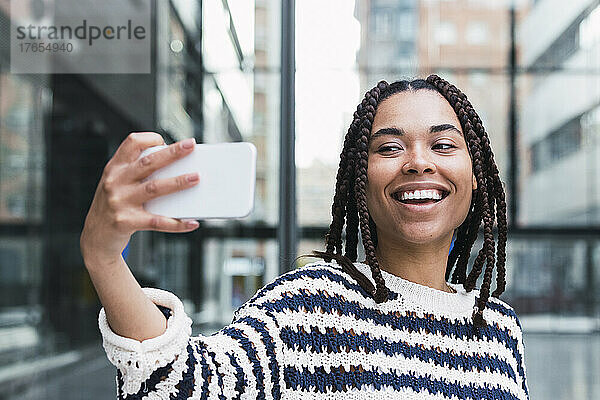 Happy young businesswoman taking selfie through mobile phone at office park