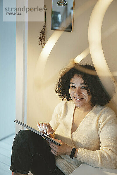 Glückliche Frau mit Tablet-PC sitzt zu Hause