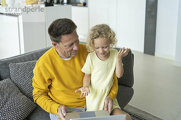 Lächelnder Vater und Tochter mit Laptop sitzen zu Hause auf dem Sofa