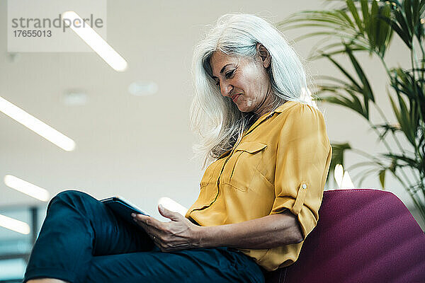 Lächelnde berufstätige Frau mit Tablet-PC im Büro sitzend
