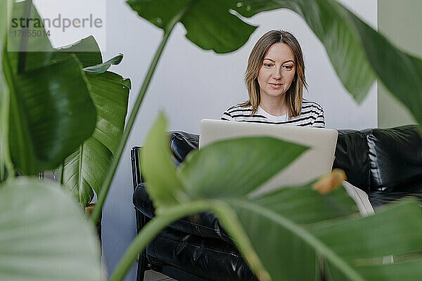 Lächelnde Frau mit Laptop sitzt auf dem Sofa