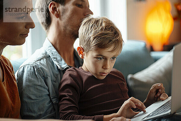 Blonder Junge benutzt Laptop und sitzt mit seinen Eltern zu Hause